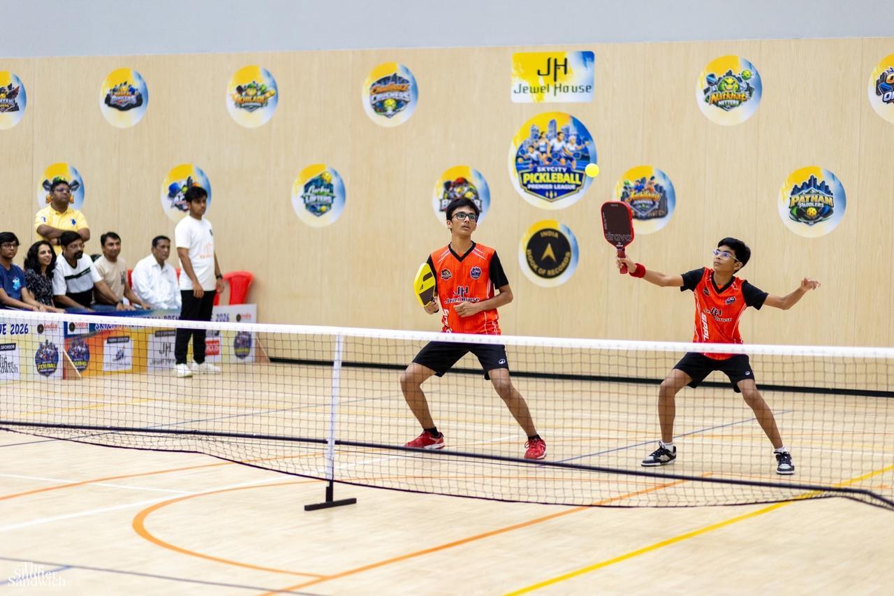 Doubles match — players in ready stance during a rally, audience watching